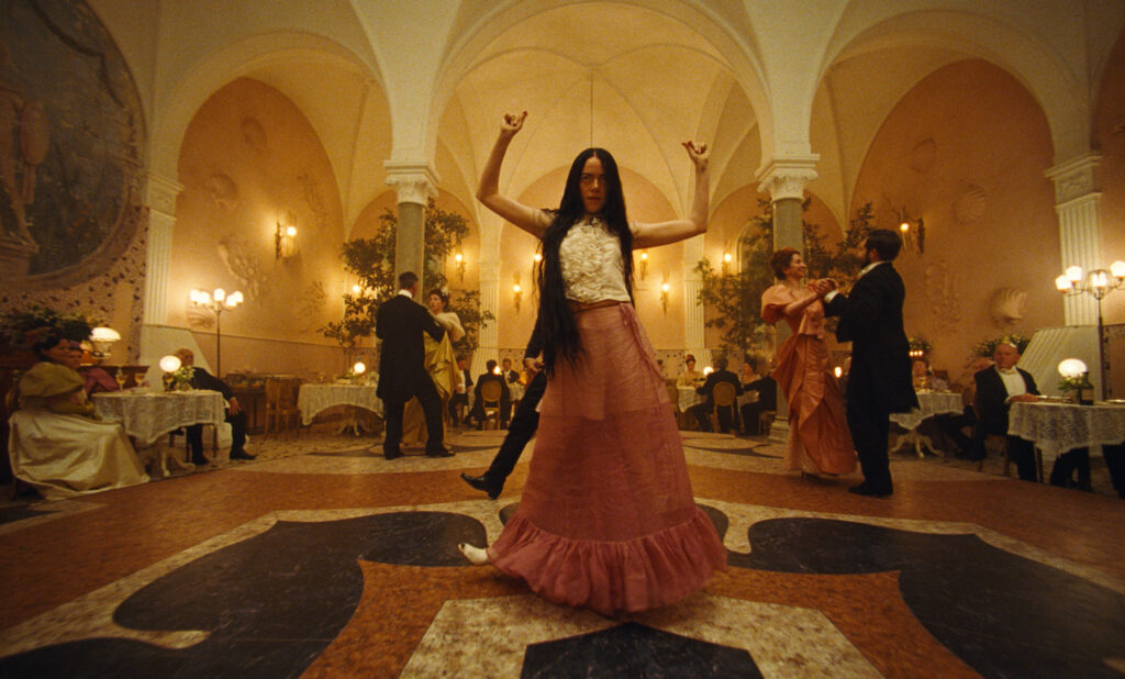 Stone, wearing a flowing peach skirt and white top and her long brown hair loose, dances in the middle of an ornate restaurant, snapping her raised fingers.