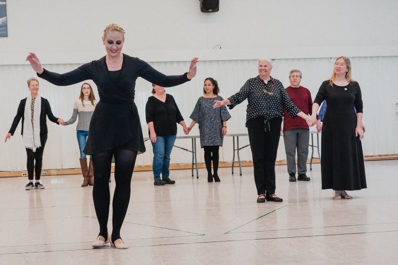 a female instructor wearing all break instructing a group of older dancers in a studio