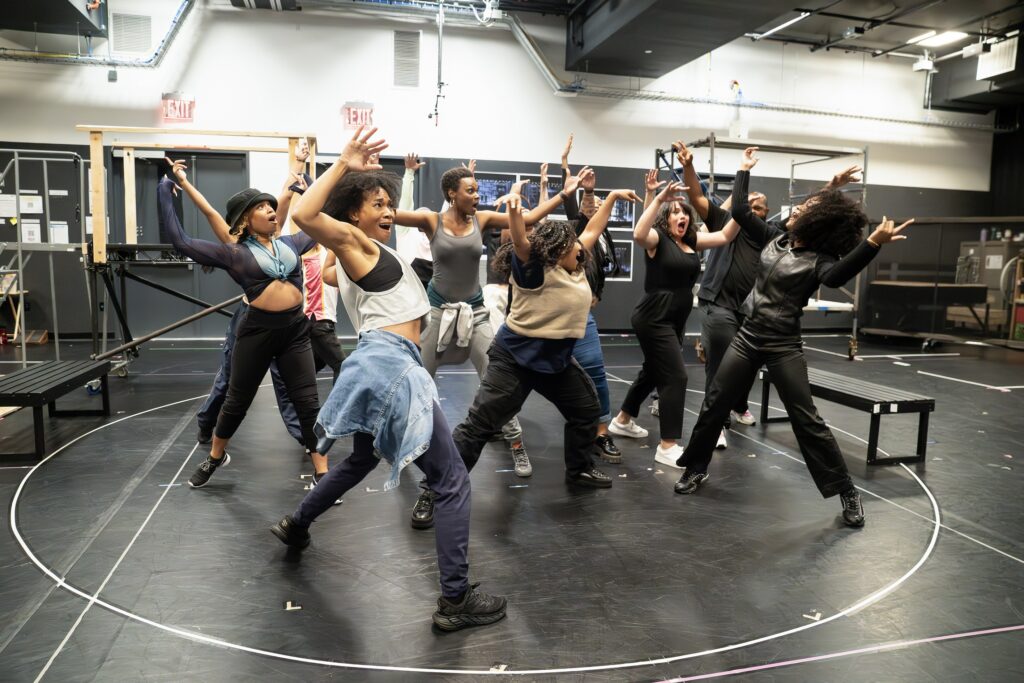a group of dancers lifting their arms over their head in a large rehearsal room