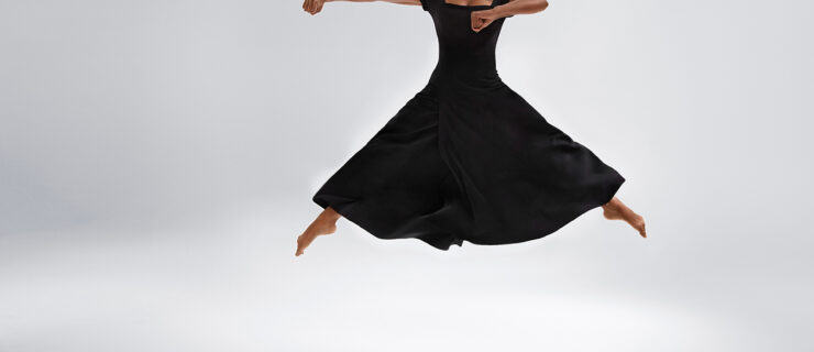 a female dancer wearing a long black dress jumping with her legs out in second