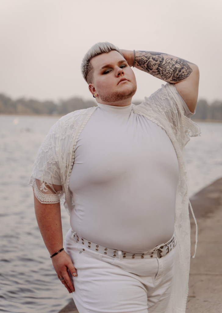 a male dancer wearing all white standing in front of a body of water