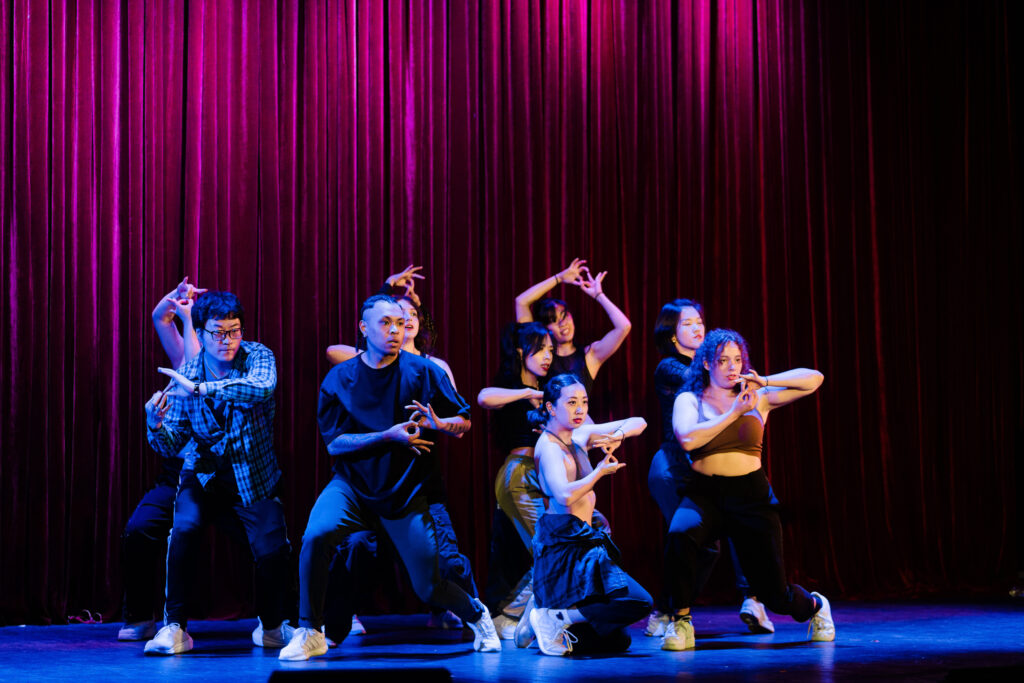 a group of adult hip hop dancers posing on stage in front of a red curtain
