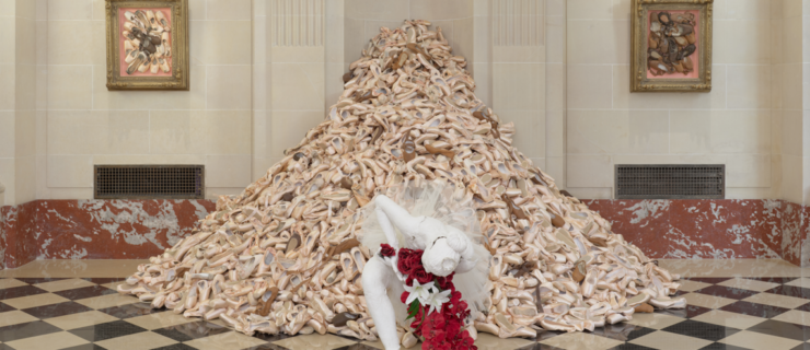 a large pile of pointe shoes with a bowing female ballerina mannequin in front of it
