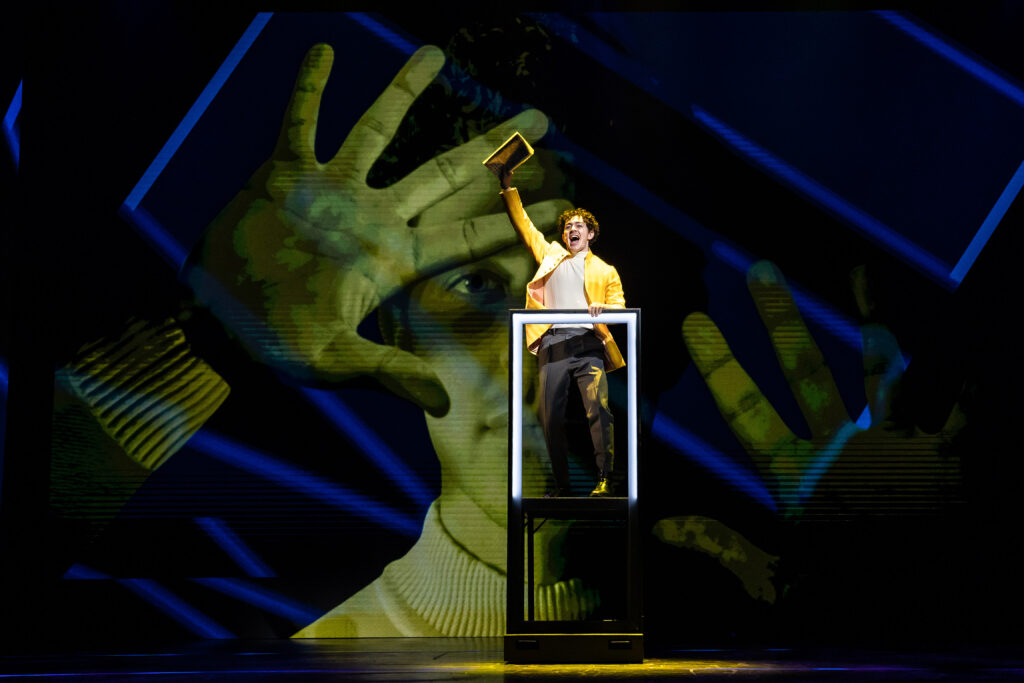 a man standing on a platform holding a book up in the air with a large projection behind him