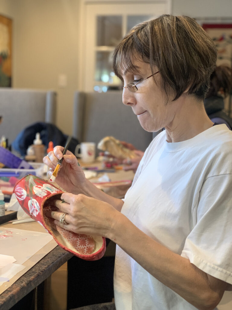 an artist painting a pointe shoes red with flowers 