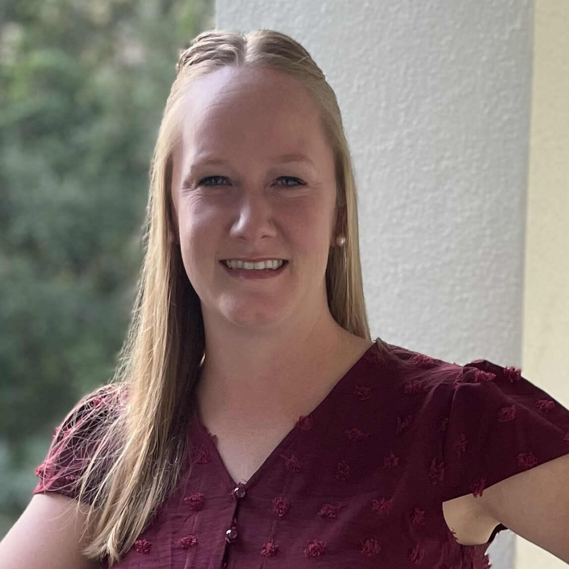 a blonde woman in a red shirt smiling at the camera 