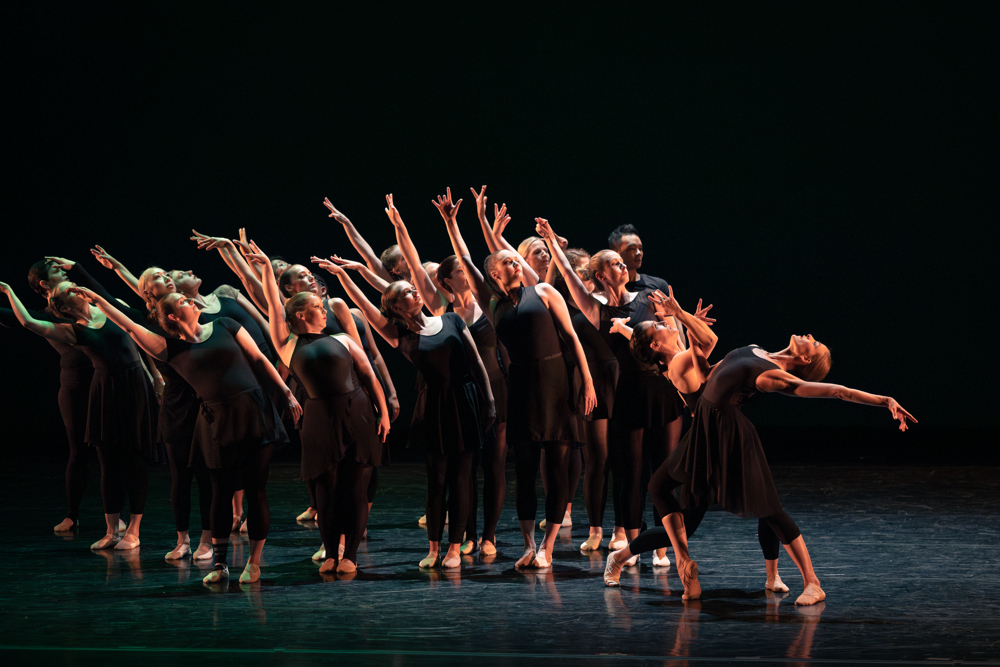 a large group of female dancers wearing all black dancing together on stage