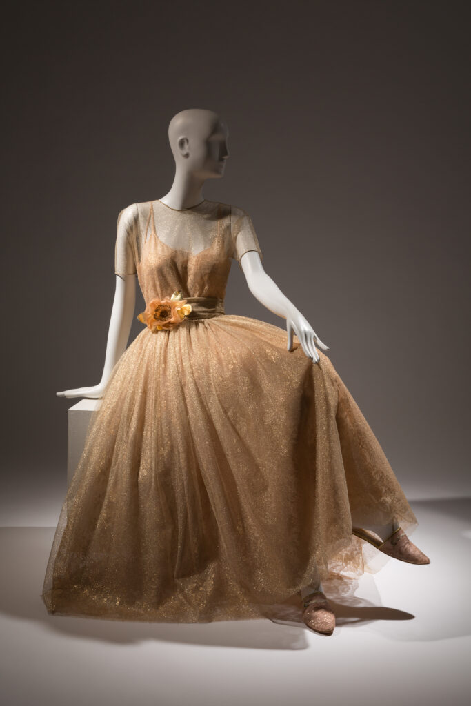 a mannequin sitting wearing a gold floor length tulle dress