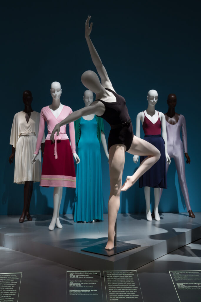 a dancing mannequin wearing a black leotard with standing mannequins behind it wearing different style dresses