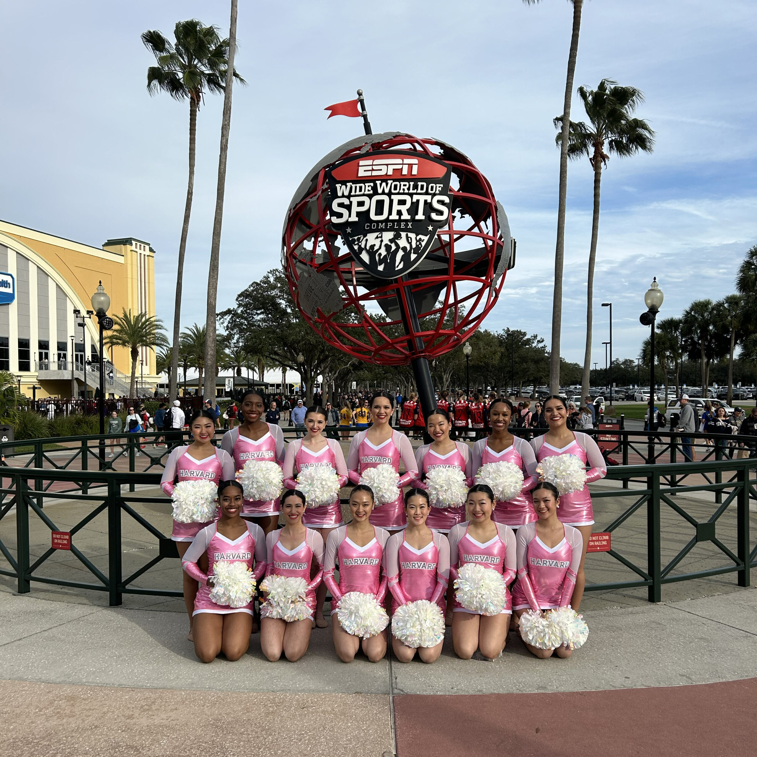 a group of dancers wearing pink uniforms and holding white poms smiling in front the Wide World of Sports logo