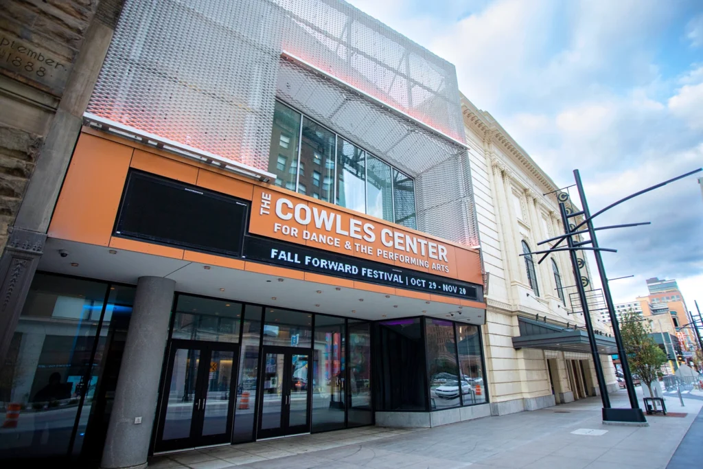 The exterior facade of The Cowles Center. The sign on the orange facade reads "The Cowles Center for Dance and the Performing Arts," and the marquee reads, "Fall Forward Festival."