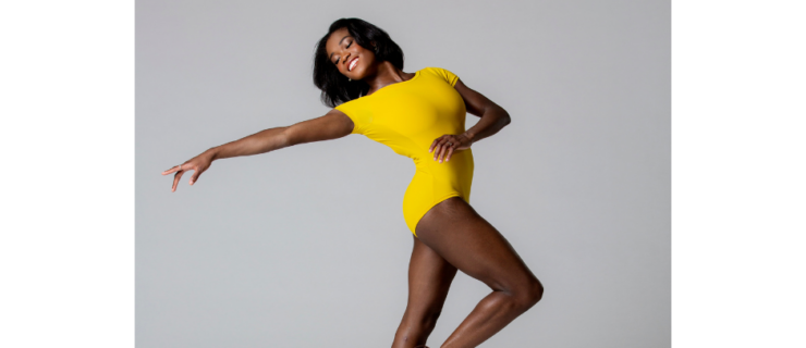 a female dancer wearing a yellow leotard dancing en pointe in front of a white backdrop