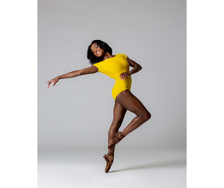 a female dancer wearing a yellow leotard dancing en pointe in front of a white backdrop