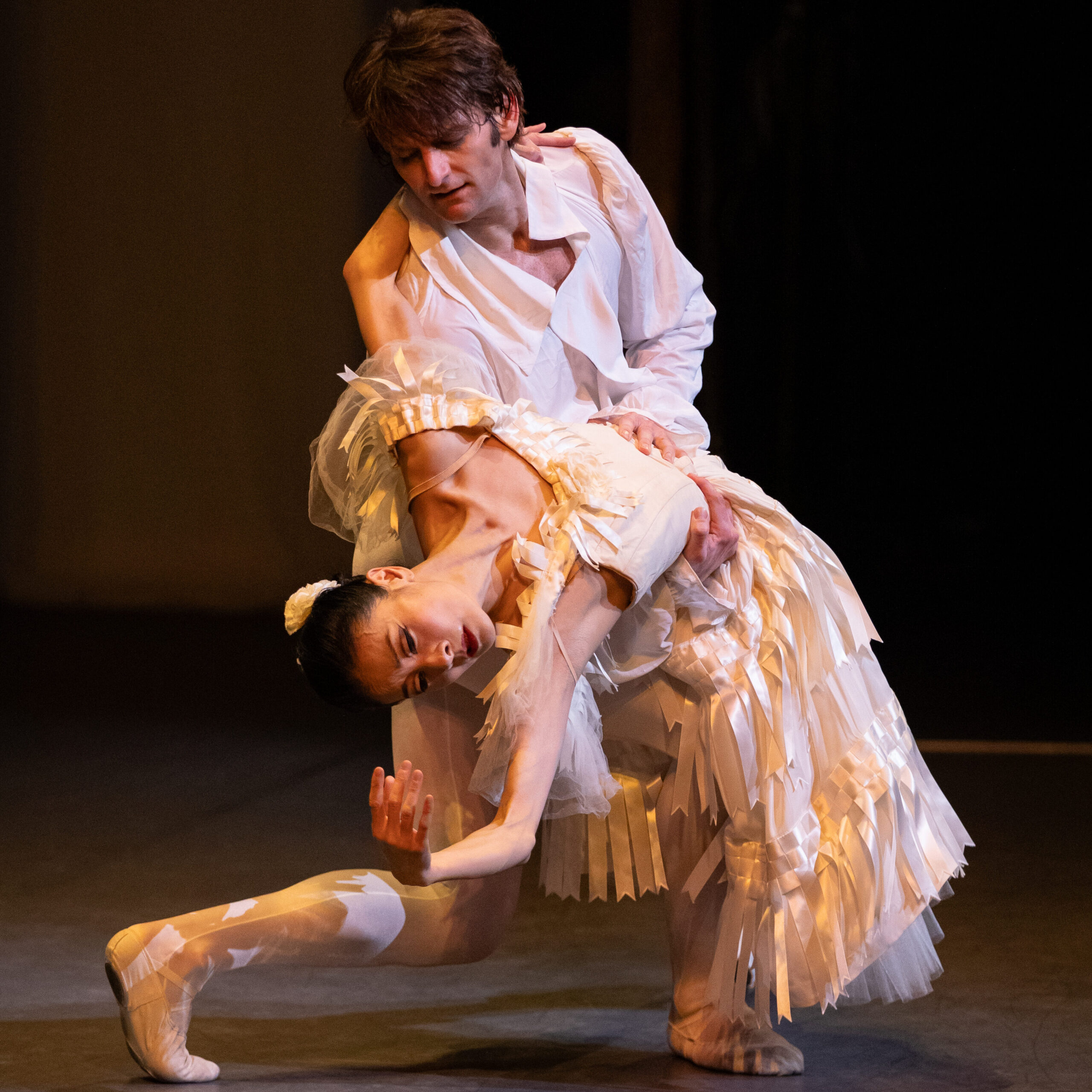 a male dancer dipping a female dancer back, both wearing white