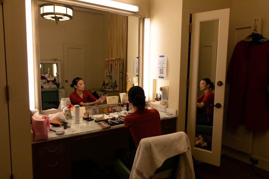 a woman sitting in a dressing room putting on makeup 