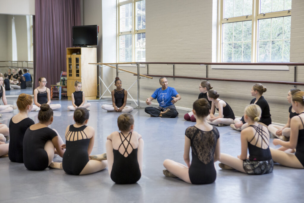 a female instructor addressing a circle of young dancers in a studio